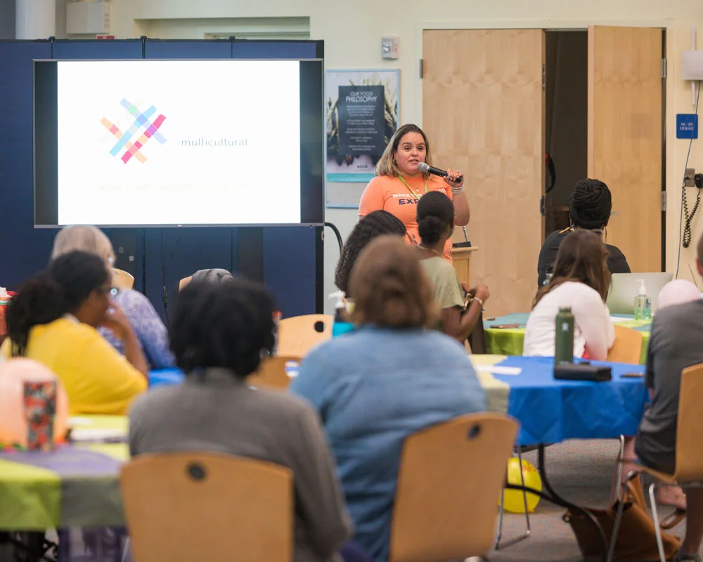 woman in orange shirt speaking into microphone