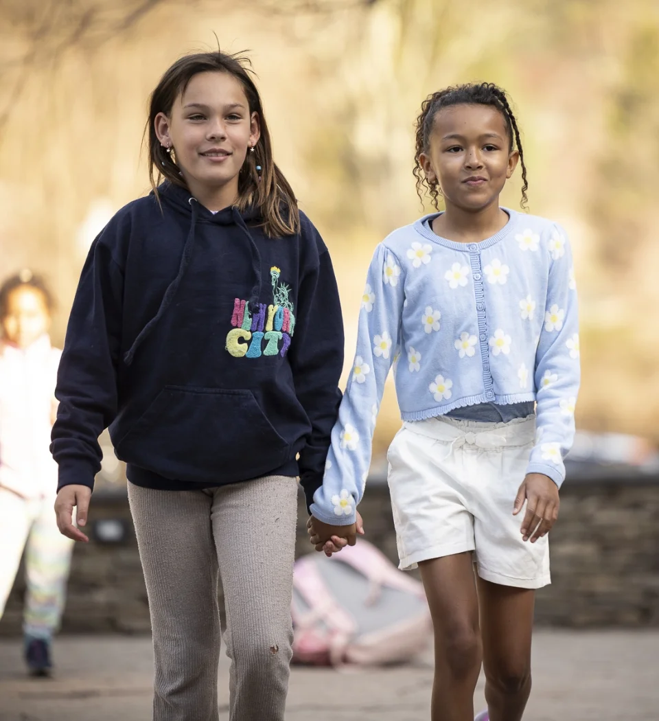 2 girls walking through campus holding hands