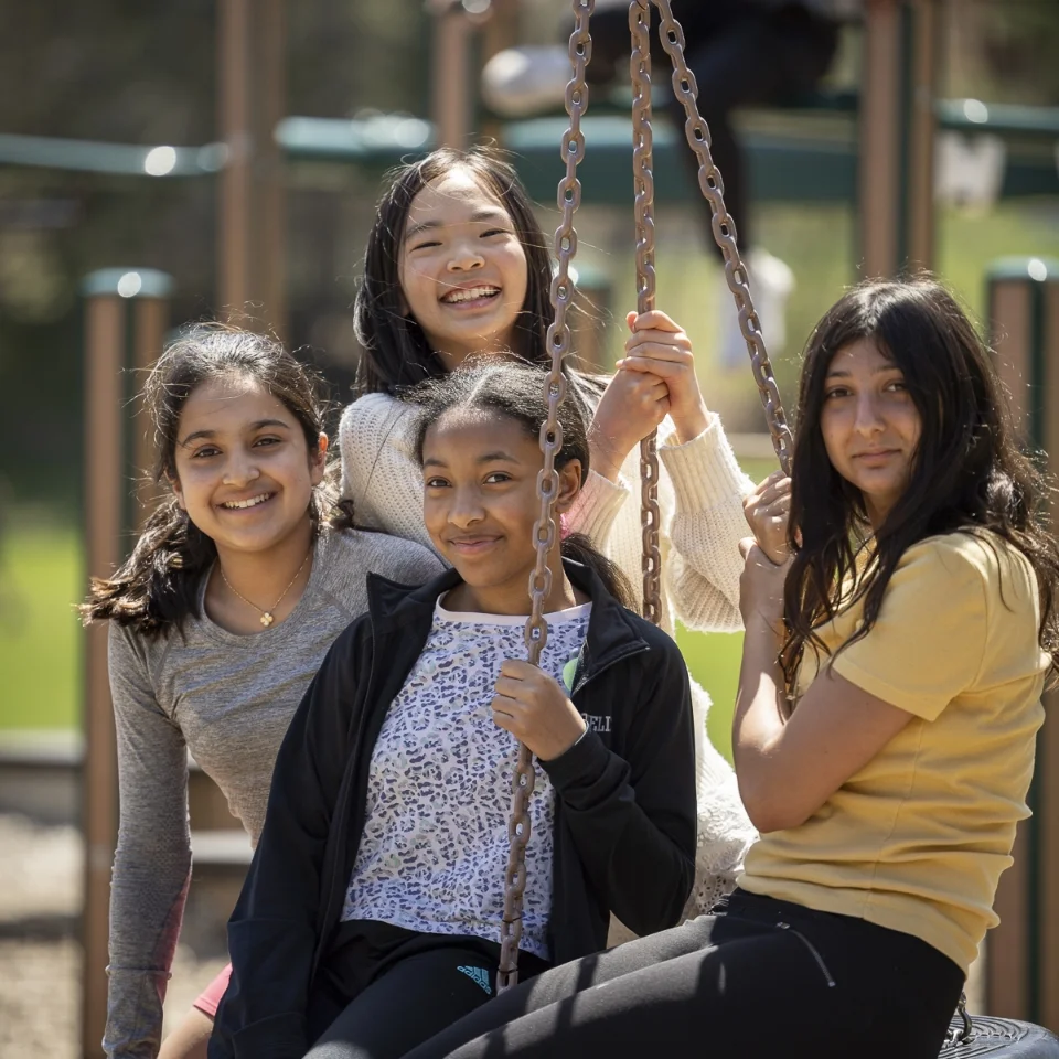 4 students sitting on a tire swing