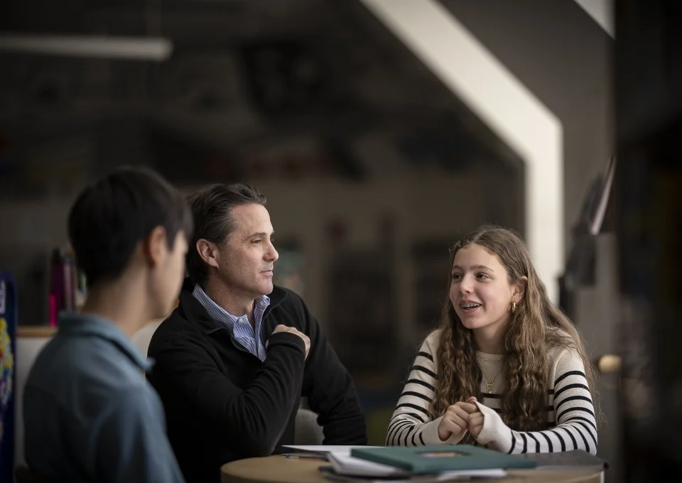 teacher and 2 students sitting at a table talking